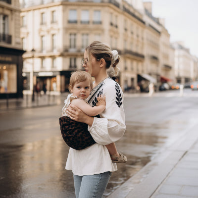 Maman portant bebe avec une echarpe de portage leopard