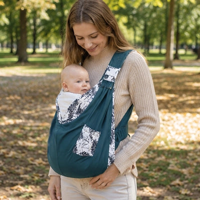 Maman porte son bébé dans une écharpe de portage florale bleue au parc.
