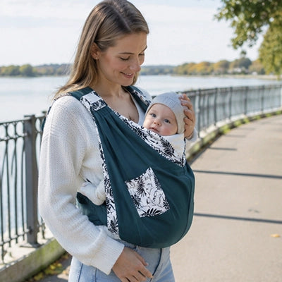 Maman se promène avec son bébé dans une écharpe de portage florale bleue.