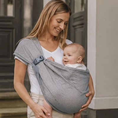 Maman porte son bébé dans une écharpe de portage fusion grise.