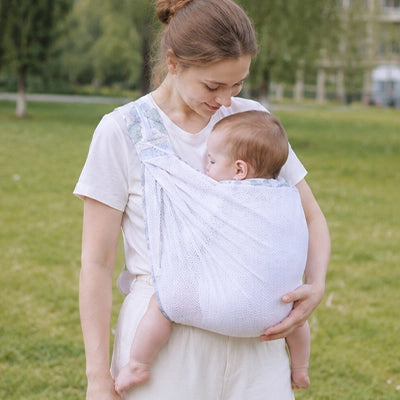 Maman se promène avec son bébé dans une écharpe de portage Pastel blanche.